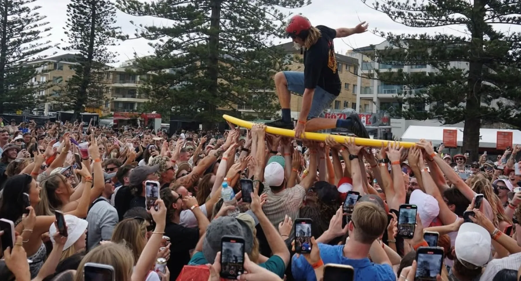 A Good Kid surfs the crowd on a yellow surfboard held up by hundreds of hands